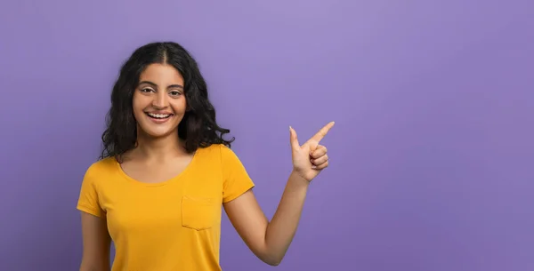 オムギ クールオファー 紫色のスタジオの背景の上に隔離された自由なスペースを指す幸せな若いインドの女性 広告や宣伝テキスト バナーのコピースペースと場所を示すエキサイティングな女性 — ストック写真