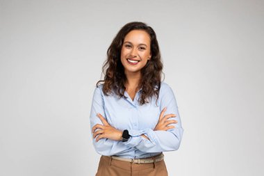 Güler yüzlü, kendine güvenen bin yıllık beyaz bayan yönetici göğsünde çapraz kollar olan resmi giysili öğretmen, arka planda gri bir arka plan stüdyosu var. Çalışma, öğrenim, kurslar ve iş