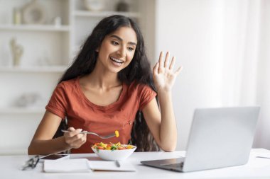 Neşeli, çekici, bin yıllık Hintli kadın ev ofisinde öğle yemeği molası veriyor, dizüstü bilgisayarın önünde oturuyor, sağlıklı sebze salatası yiyor, erkek arkadaşı ya da ailesiyle görüntülü görüşme yapıyor,