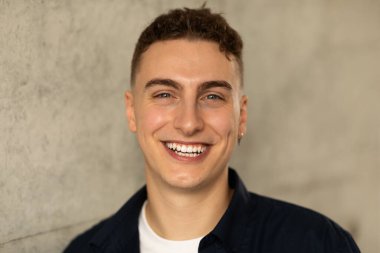 Bin yıllık beyaz bir erkek öğrencinin portresi. Şehrin gri duvarındaki kameraya gündelik bir şekilde bak. Açık havada, kapat. İş, iş, öğrenim ve eğitim, reklam ve teklif