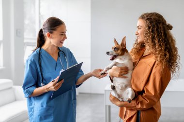Veteriner dostça notlar alan, olumlu veterinerlik ziyareti ve evcil hayvan bakımı etkileşimini resmeden, veteriner ile veteriner danışma sırasında kadın sahibinin tuttuğu köpek.