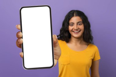 Heyecanlı, neşeli, kıvırcık, Hintli kız öğrenci elinde beyaz ekranla kocaman bir telefon gösteriyor. Güzel bir online teklif, anlaşma, mor stüdyo geçmişi öneriyor. Mobil uygulama