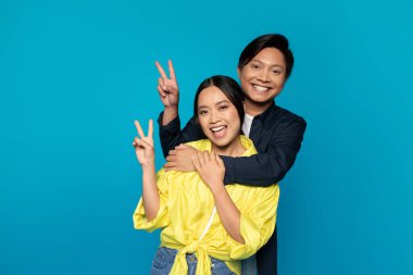 Gülümseyen Koreli genç adam sıradan bir barış işareti ile bayana sarılıyor, ilişkilerinin keyfini çıkarıyor, mavi stüdyo geçmişinde soyutlanıyor. Romantik eğlenceli fotoğraf, randevu ve aşk, reklam ve teklif