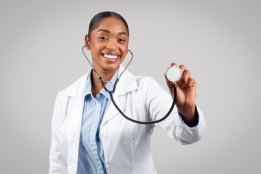 Gülümseyen bin yıllık Afro-Amerikan kadın doktor steteskop, teşhis hastası, sağlık muayenesi gri arka planda, stüdyoda izole edilmiş. Sağlık hizmetleri, sağlık
