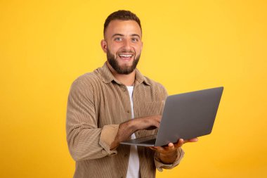 Bin yıllık neşeli beyaz adam yöneticisi iş için dizüstü bilgisayarda yazı yazıyor, iş sohbeti yapıyor, turuncu stüdyo arka planında izole edilmiş. Uzaktan eğitim, reklam ve teklif, serbest ve pazarlama