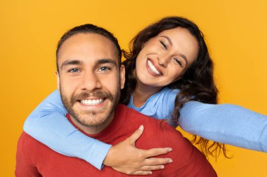 Mutlu, sevgi dolu bir yüzyılın yakın plan portresi. Birlikte selfie çekiyorlar, sarı stüdyo duvarında poz veriyorlar. Neşeli genç kadın erkek arkadaşını sırtında taşıyor, fotoğraf çekiyor.