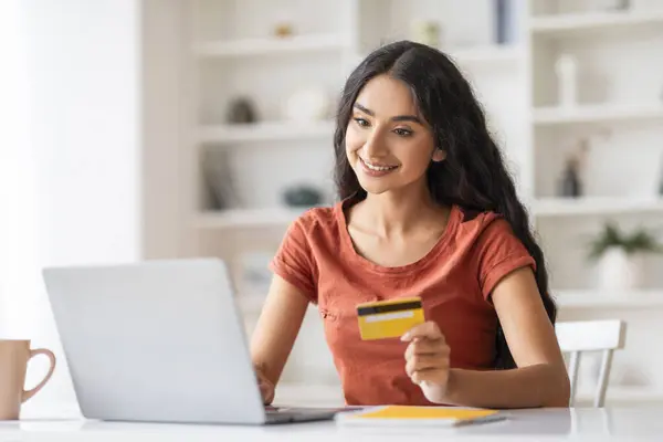 Young indian woman holding credit card and using laptop computer. Businesswoman working at home. Online shopping, e-commerce, internet banking, spending money, working from home concept