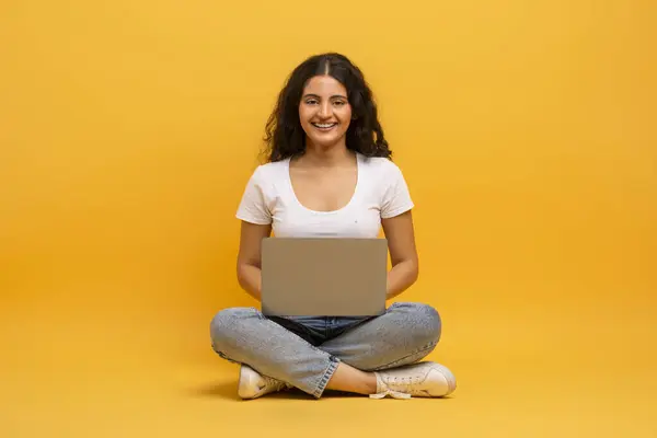 黄色いスタジオの背景の上にラップトップウェブサーフィンシッティングを使用して幸せな若いインドの女性 コンピュータでオンラインで働く東部の女性のショット 技術とインターネット — ストック写真