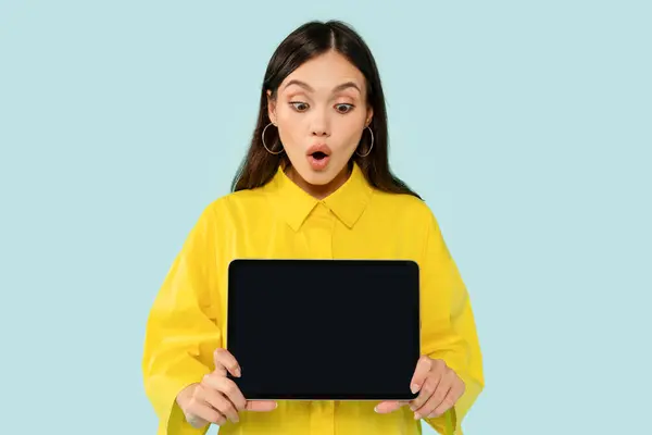 黒い空のスクリーンが付いているデジタルタブレットを示す黄色いシャツを身に着けている驚くべきかわいいブルネットの若い女性はショックを受けた顔の表情 素晴らしいモバイルアプリ オンラインオファー モックアップ — ストック写真