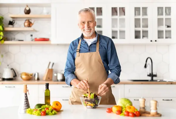 Portrait Of Handsome Mature Chef Man In Apron Posing In Kitchen Interior, Happy Senior Gentleman Cooking Healthy Food At Home, Mixing Vegetables In Bowl And Smiling At Camera, Copy Space