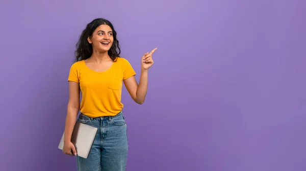 リモート ジョブ チャンス フリーランス 彼女の手でラップトップとカジュアルな服を着て陽気でかわいいインドの若い女性学生 コピースペースを指して 紫色の背景 パノラマ — ストック写真