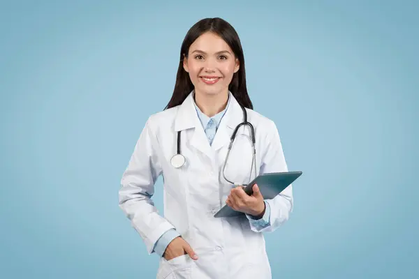 年轻自信的女医生 脖子上戴着听诊器 手持数码平板电脑 准备接受治疗 背景为蓝色 — 图库照片