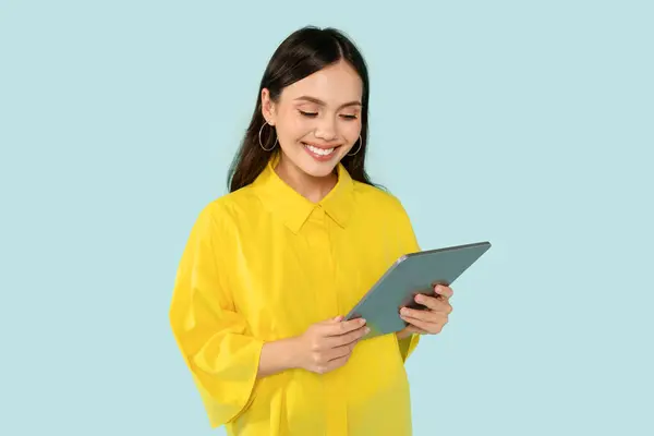 穿着黄色衬衫的快乐漂亮的年轻女性 在蓝色的工作室背景下显得孤立无援 使用现代Pc数码平板电脑 查看好的教育或娱乐移动应用 复制空间 — 图库照片