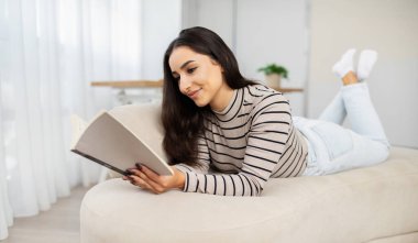 Mutlu, sakin, genç, güzel Arap kadın kitap okur, plan yapar, oturma odasının iç tarafındaki kanepede uzanır. Bayan boş zaman, eğitim, eğitim, hobi ve evde rahat bir yaşam sürüyor.