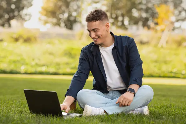 Glad millennial caucasian man enjoy lifestyle and rest, typing on laptop, relax in park, sit on grass. Work, business, study with technology, freelance outdoor, break at free time, digital nomad