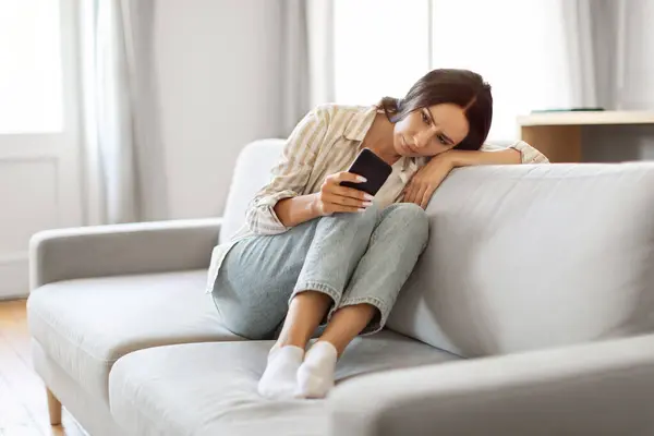 Jovem Mulher Perturbada Olhando Para Tela Smartphone Sentada Sofá Casa — Fotografia de Stock