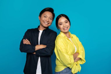 Neşeli, kendine güvenen genç Çinli kadın ve erkek, göğsünde çapraz kollar, mavi stüdyo geçmişinde soyutlanmış. Reklam ve teklif, ilişkiler ve aşk, profesyonel tavsiye