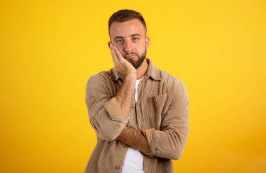 Yorgun, hasta, genç Avrupalı bir adam sarı stüdyo arka planında el ele, dinlenmeye, izole bir şekilde sıkışıyor. Aşırı çalışma, insanların duyguları ve yaşam tarzı, yüz ifadesi, uykusuz, uykusuz