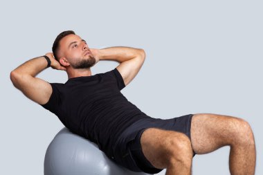 Sakallı, kaslı, genç Avrupalı bir adam, spor giyim kuşamları, gri stüdyo arka planında izole edilmiş, formalı karın kasları için egzersiz yapıyor. Vücut bakımı ve kilo kaybı eğitimi