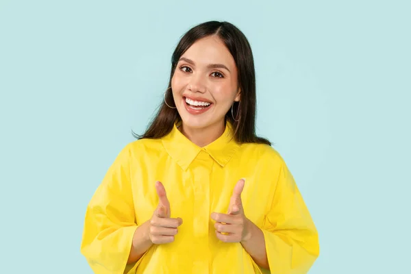 ポジティブな陽気で魅力的な若い女性は カメラで指摘し カメラで微笑んでいることを示す黄色のシャツを着て かなりミレニアルな女性は 青いスタジオの背景にポーズ — ストック写真