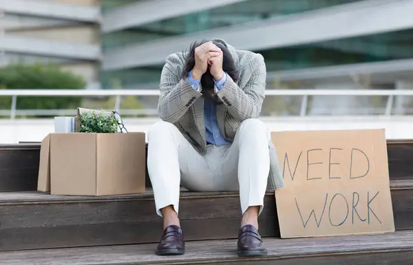 不快乐的日本商人手牵着头坐在外面 旁边的纸板标牌是 需要工作 属于办公室的盒子 在城市地区的室外 失业和解雇 — 图库照片