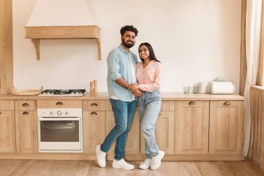 Sevecen Hintli çift, güneşli, ferah mutfaklarında ahşap dolaplar ve modern aletlerle el ele tutuşuyorlar.