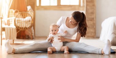 Küçük oğluyla yoga yapan genç bir kadın. Spor yapan bir bayan. Vücut esneme egzersizi yapıyor. Oturma odasında jimnastik yapıyor.
