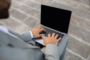 Tanımlanamayan iş adamı laptopta boş ekran açık havada çalışıyor takım elbiseli bir erkek girişimci, şehir merkezinde merdivenlerde oturuyor, web sitesini tarıyor, maket yapıyor.