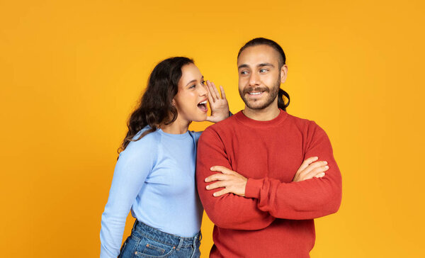 Привлекательная женщина тысячелетия, делящаяся секретом или шепчущая сплетни своему мужу или бойфренду, на фоне жёлтой студии. Любящая пара делится слухами. Общение в браке