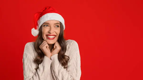 サンタハットの笑顔のヨーロッパの女性は クリスマスと新年の季節の喜びを体現し 赤いスタジオの背景に対して 予想される祭りを脇に見ます パノラマ コピースペース — ストック写真