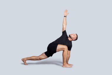 Spor giyim yogasında odaklanmış beyaz bir genç, vücut esneme hareketleri, nefes egzersizleri, dengenin tadını çıkarma, gri stüdyo arka planında izole edilmiş, tam boy. Sağlık, spor ve barış