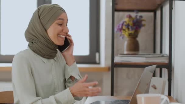 喜びをもってビジネス交渉 ヒジャブの若い肯定的なイスラム教徒の女性はビジネスパートナーと話し ラップトップ上の文書を議論し 自宅のオフィスで楽しいトークを楽しんでいます — ストック動画