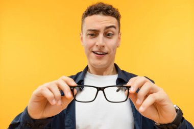 Stüdyoda, sarı arka planda duran, gözlüğünü takan, göz makyajına ve suratını buruşturan neşeli, neşeli, yakışıklı bir genç adam var. Görüş, göz bakımı
