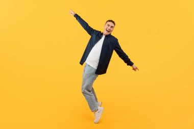 Pozitif yakışıklı genç adam sarı stüdyo arkasında poz veriyor, hareketli dans ediyor ve gülümsüyor, mutlu hippi adam hayatın tadını çıkarıyor, tam boy, kopyalama alanı.