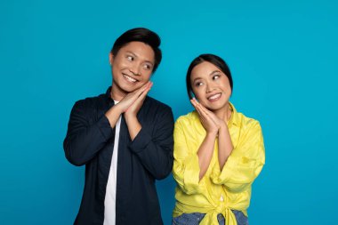 Mavi stüdyo arka planında soyutlanmış, sıradan bakışlarıyla gülümseyen genç bir Japon adam ve kadın. Flört, romantik randevu ve aşk, hassas an, birlikte ilişkiler.