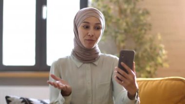 Uzaktan çalışma konsepti. Genç profesyonel islami kadın İK yöneticisi başvuru sahibi ile online görüşme yapıyor, ev telefonuyla görüntülü görüşme, izleme çekimi, yavaş çekim.