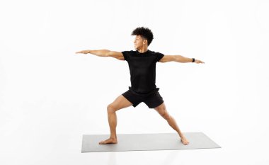 Brezilyalı fitness eğitmeni yoga savaşçısı pozu veriyor, dengeli ve güçlü, spor kıyafeti giyiyor, sağlıklı ve sağlıklı yaşam tarzını destekliyor, beyaz stüdyo arka planında