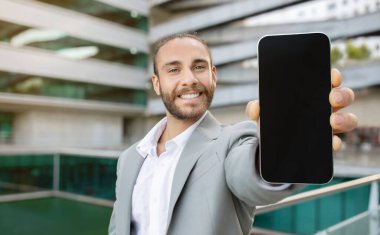 Takım Elbiseli Yakışıklı Genç İşadamı Kamerada Büyük Boş Akıllı Telefonu Gösteriyor, Heyecanlı Milenyum Erkek Girişimcisi Yeni Mobil Uygulama Tavsiye Ediyor, Açık havada İş Merkezi Yakınlarında Poz Veriyor, Mockup