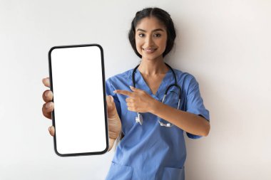 Hintli doktor kadın elinde beyaz ekranlı, mavi önlüklü akıllı telefonu işaret eden, üniformalı genç terapist, tıbbi reklamlar için fotokopi alanı sunan,