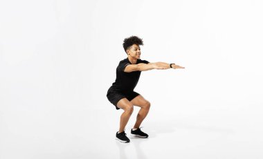 Spor yaparken kollarını uzatan atletik genç bir adam spor yaparken çömeliyor, bacak dayanıklılığı üzerinde çalışıyor, forma giyiyor, beyaz stüdyo arka planında egzersiz yapıyor. Boş boşluklu fitness pankartı