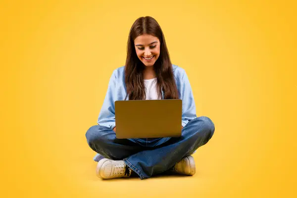 令人高兴的是 高加索少年女学生使用电脑 坐在地板上 隔离在黄色背景下 工作室 在线学习 远程教育和教学 — 图库照片