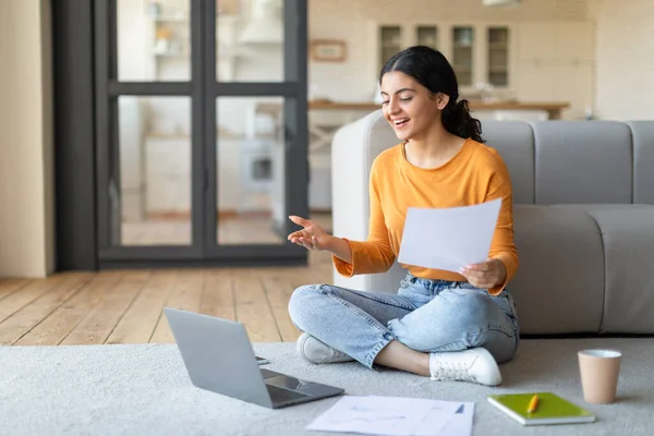 Remote Career. Smiling Young Indian Woman Using Laptop For Video Call At Home, Millennial Eastern Female Holding Papers And Talking At Web Camera, Making Teleconference On Computer, Copy Space