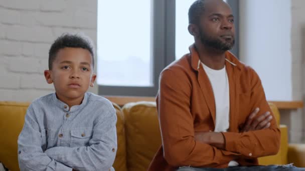 世代間ギャップ 怒ったアフリカ系アメリカ人の父親と息子は 折り畳まれた腕でソファーに座り お互いを見つめ合い 自宅でお互いに背を向ける — ストック動画