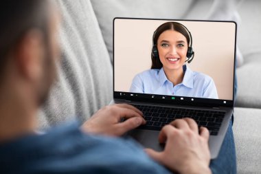 Oturma odasındaki kanepede dinlenen bir adamın video ekranlı en yeni laptopunu kullanırken, neşeli genç bayan teknik destek ya da finansal danışman ile görüntülü konuşma yaparken omuz üstü görüntüsü.