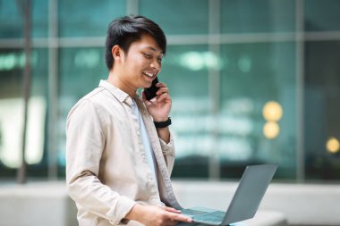 Genç Filipinli girişimci dizüstü bilgisayar kullanıyor ve şehir merkezindeki müşteriyle telefonda konuşuyor. İş toplantısını, yan görüşü, kopyalama alanını beklerken birden fazla iş yapıyor.