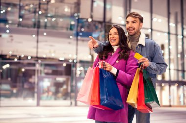Neşeli alıcılar kredi kartlarını modern alışveriş merkezinin dışında alışveriş için hazır tutuyorlar. Yeni yıl indirimi ve boş alana işaret ediyorlar.