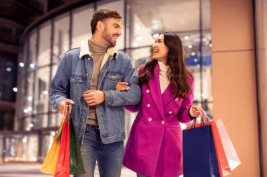 Neşeli müşteriler kışın neşeli akşam yürüyüşlerine çıkarlar, alışveriş torbalarıyla gülümserler, Noel indirimlerinin tadını çıkarırlar, tatil tüketimi ve moda için ideal yerler, açık hava alışveriş merkezleri.