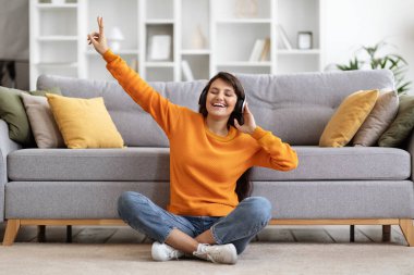 Milenyum doğusundaki olumlu kadın en sevdiği müziğin keyfini çıkarıyor, oturma odasında yerde oturuyor, kablosuz stereo kulaklıklar kullanıyor, şarkılar söylüyor ve el sallıyor, boşluğu kopyalıyor.