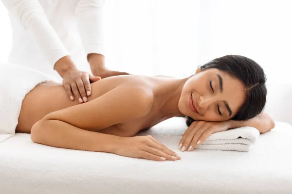 Beautiful indian woman receiving relaxing back massage from professional therapist in spa salon, closeup shot of attractive young lady enjoying wellness treatment in beauty studio