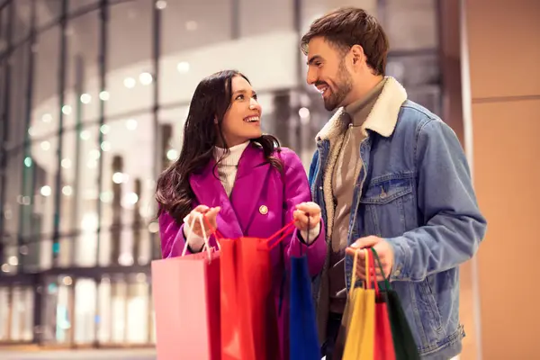 Mutlu alıcılar kış kıyafetleri içinde alışveriş merkezinin önünde alışveriş torbaları tutarak Noel alışverişi bulduklarını gösteriyorlar. Tatil tüketim kavramı
